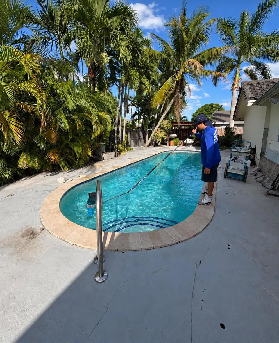 Technician vacuuming a pool surrounded by palm trees